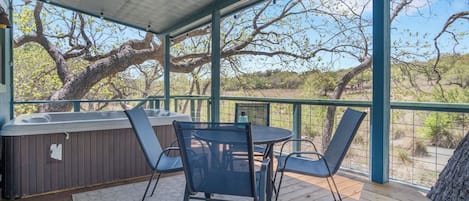 Un espacio de estar al aire libre techado con una mesa, sillas, un jacuzzi y vistas a árboles y al paisaje.