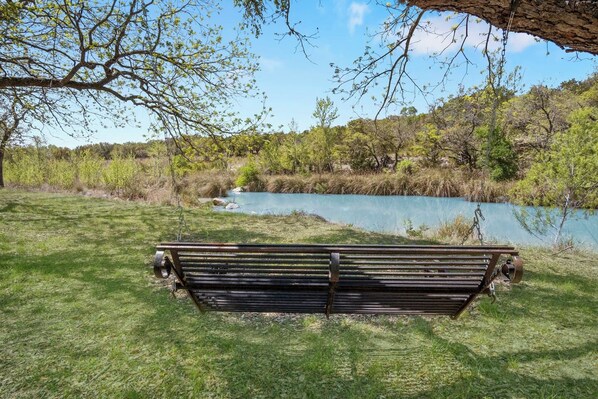 A bench in a grassy area with a view of a body of water and trees.