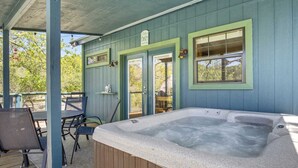 A hot tub under a covered deck with a wooden railing, a door with a sign, and a window. - Bandera Stronghold Crazy Horse (Bandera)