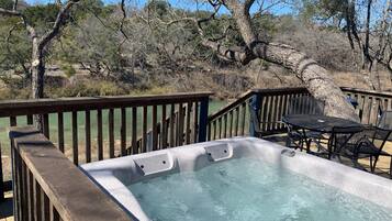 A hot tub with a wooden deck and chairs, surrounded by trees and a natural landscape.
