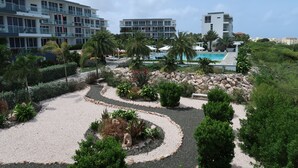 Un hotel moderno con varios pisos, un jardín ajardinado con palmeras y una piscina.