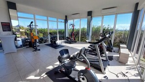Un gimnasio con máquinas de cardio, pesas y un amplio ventanal con vistas al exterior.