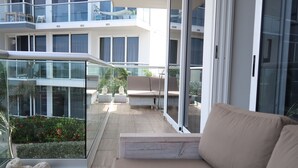 Un apartamento moderno con balcón, sofá y vistas a un jardín y otros edificios.