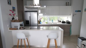 Una cocina moderna con armarios blancos, un refrigerador de acero inoxidable, un horno empotrado y una isla grande con dos taburetes blancos.