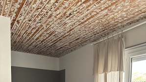 A bedroom with a bed, a window with curtains, and a ceiling with a textured pattern. - Spacieux Studio Pour Toute la Famille (Palavas-les-Flots)