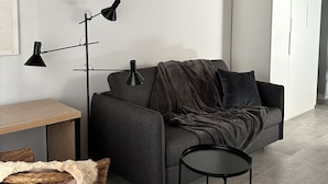 A modern living room with a grey sofa, a small round table, a floor lamp, and a wicker chair. - Spacieux Studio Pour Toute la Famille (Palavas-les-Flots)