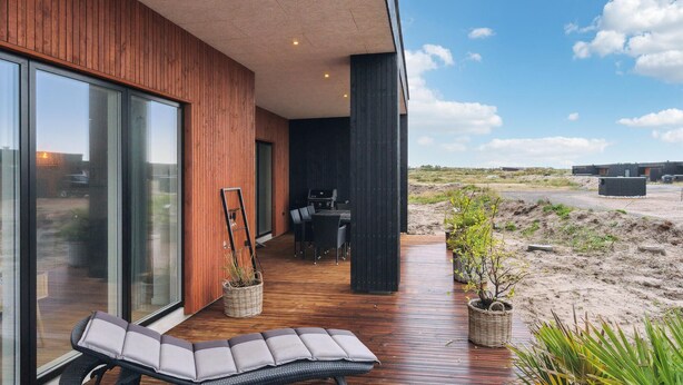 Una terrazza esterna moderna con pavimento in legno, zona salotto con panchina e barbecue.