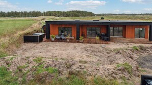 Una casa moderna con veranda in legno, ampie finestre e area salotto esterna.