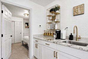 Una cocina moderna con armarios blancos, encimera de mármol, grifo dorado y cafetera.
