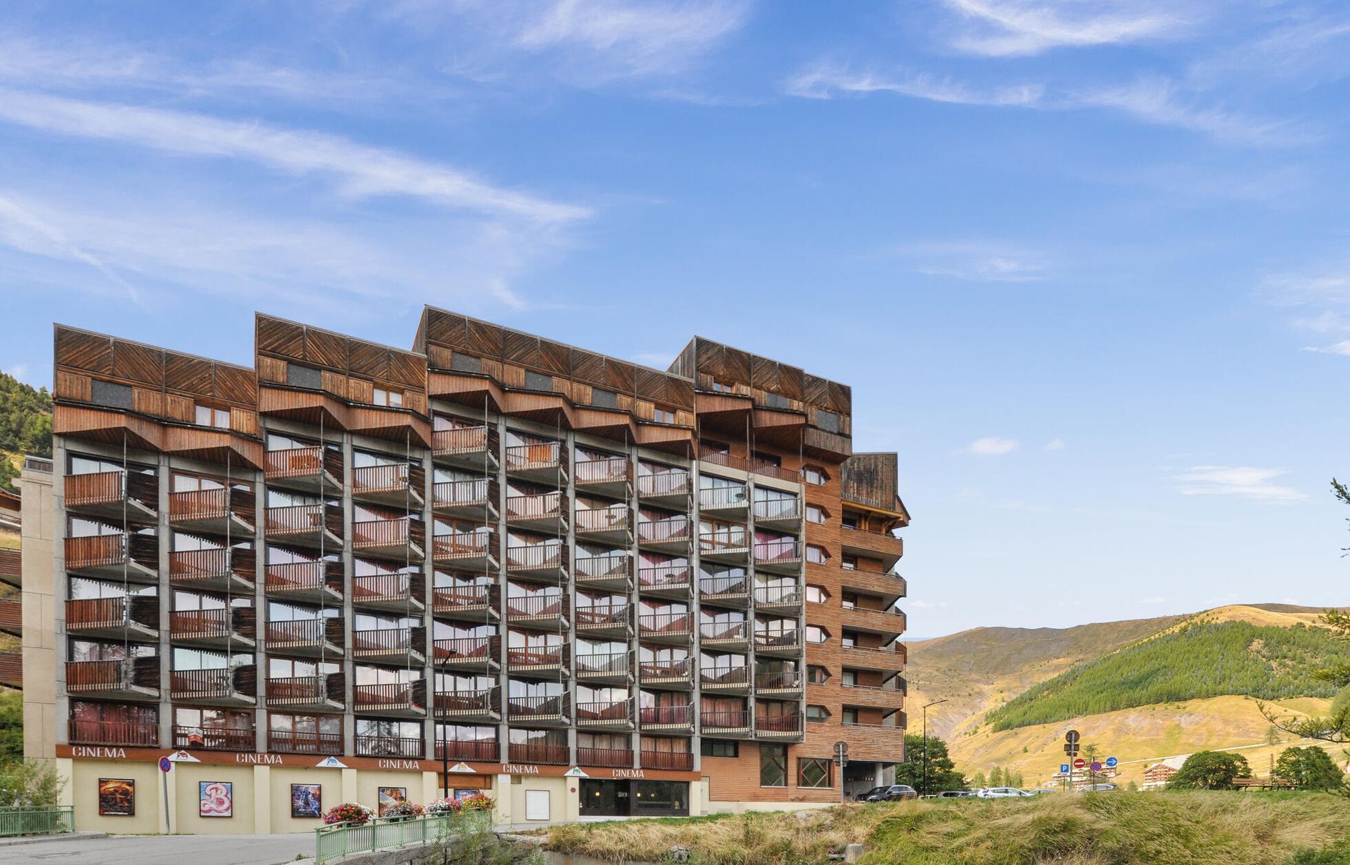 A multi-story building with balconies, a cinema sign, and a view of hills in the background.