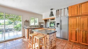 A kitchen with a brick island, wooden cabinets, a stainless steel refrigerator, and a dining area with a glass door leading outside. - Awesome home in Saint Martin de Crau (Saint Martin de Crau)