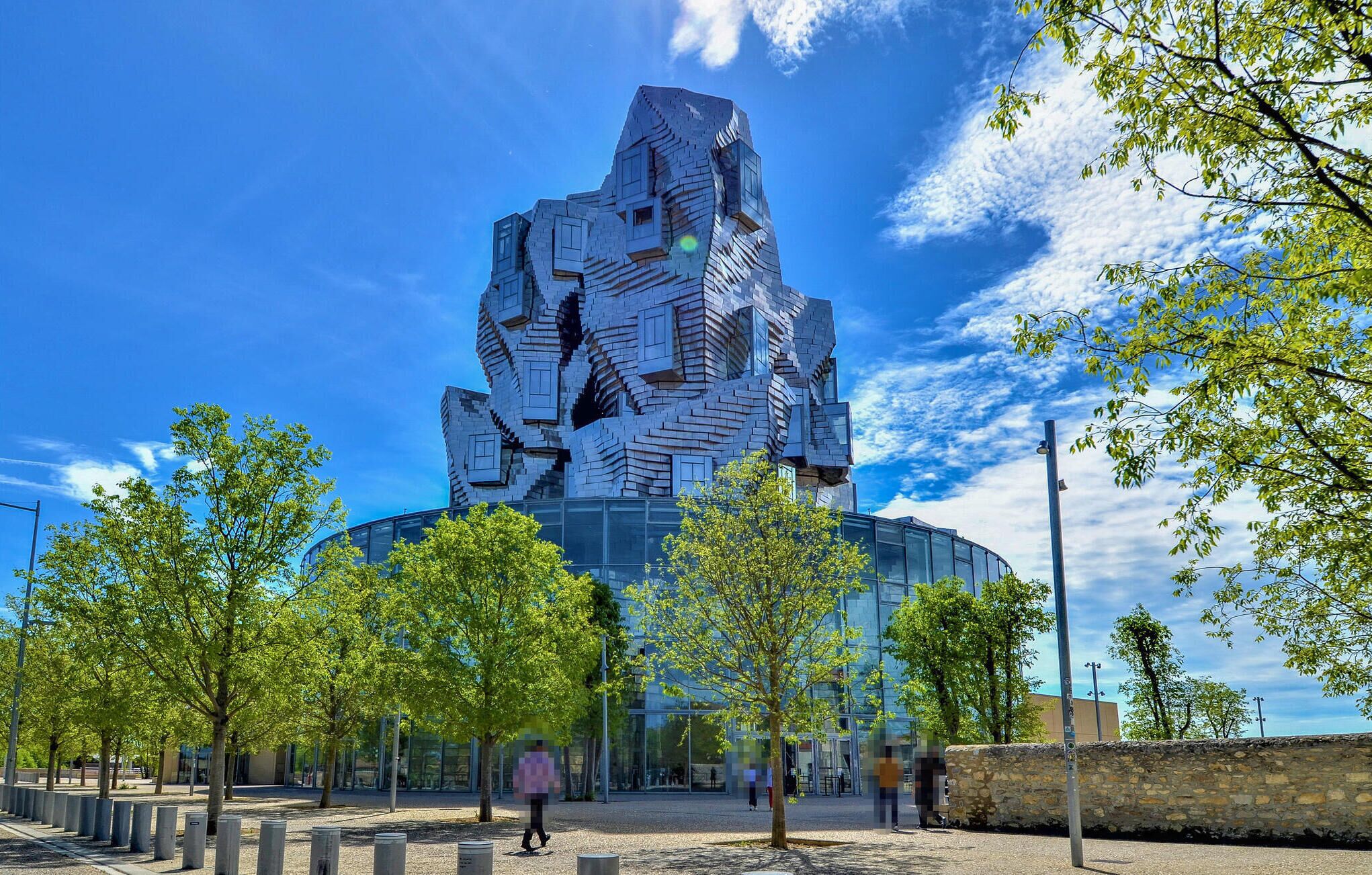 A modern building with a unique, angular design, surrounded by a park with trees and a stone wall.
