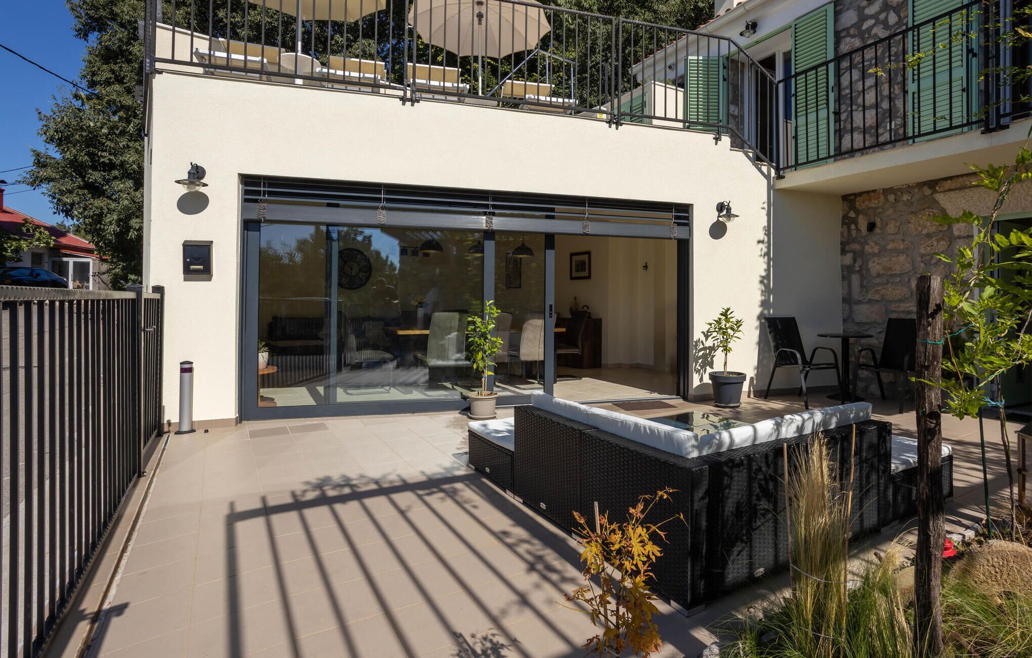 A modern house with a glass door leading to a patio area, outdoor furniture, and a stone wall.