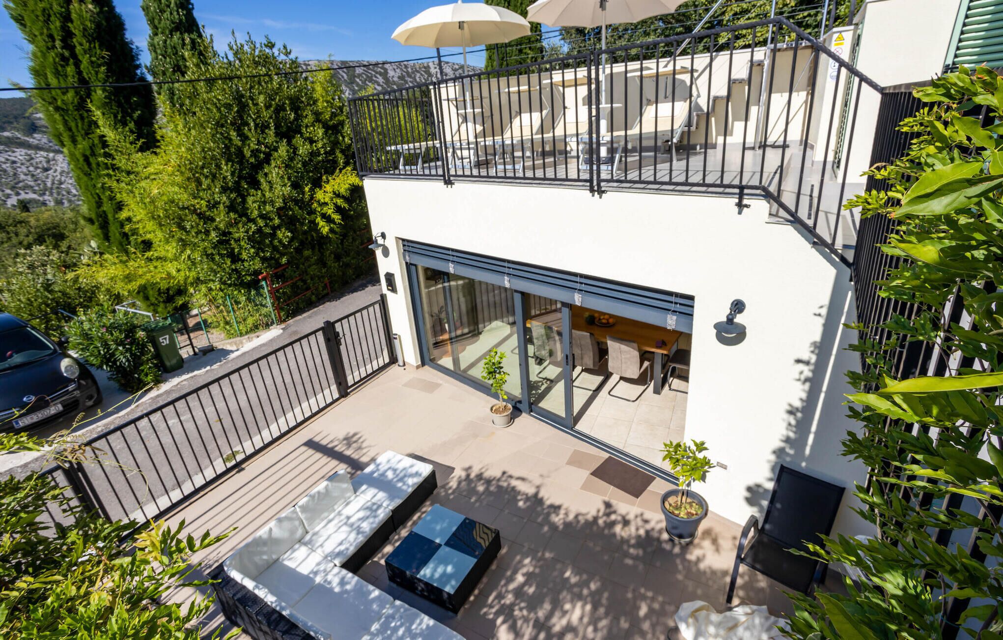 Ett modernt hus i två våningar med en balkong, utomhusmöbler och utsikt över den omgivande naturen.