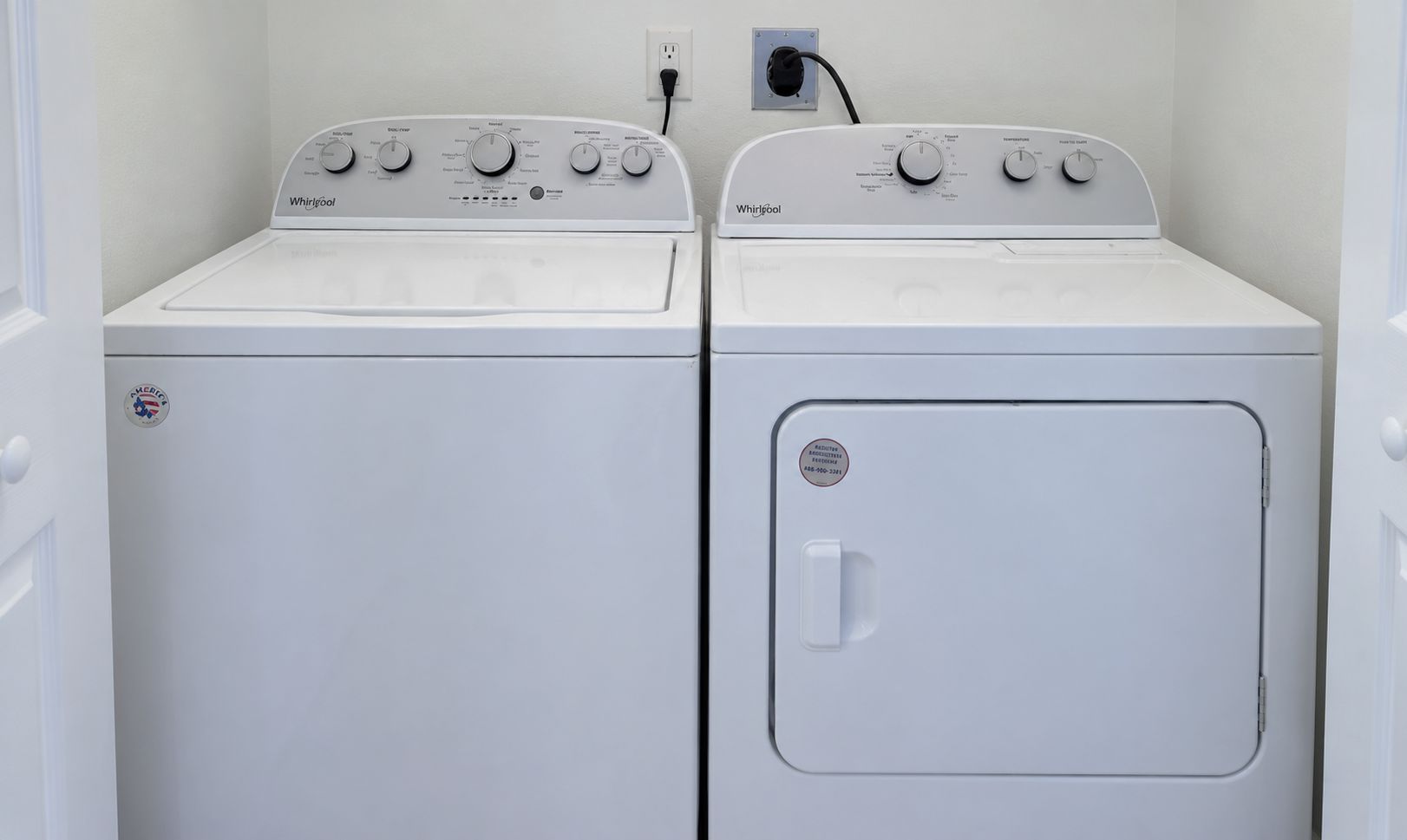 Två vita torktumlare från Whirlpool står bredvid varandra i ett tvättrum, med ett eluttag ovanför.