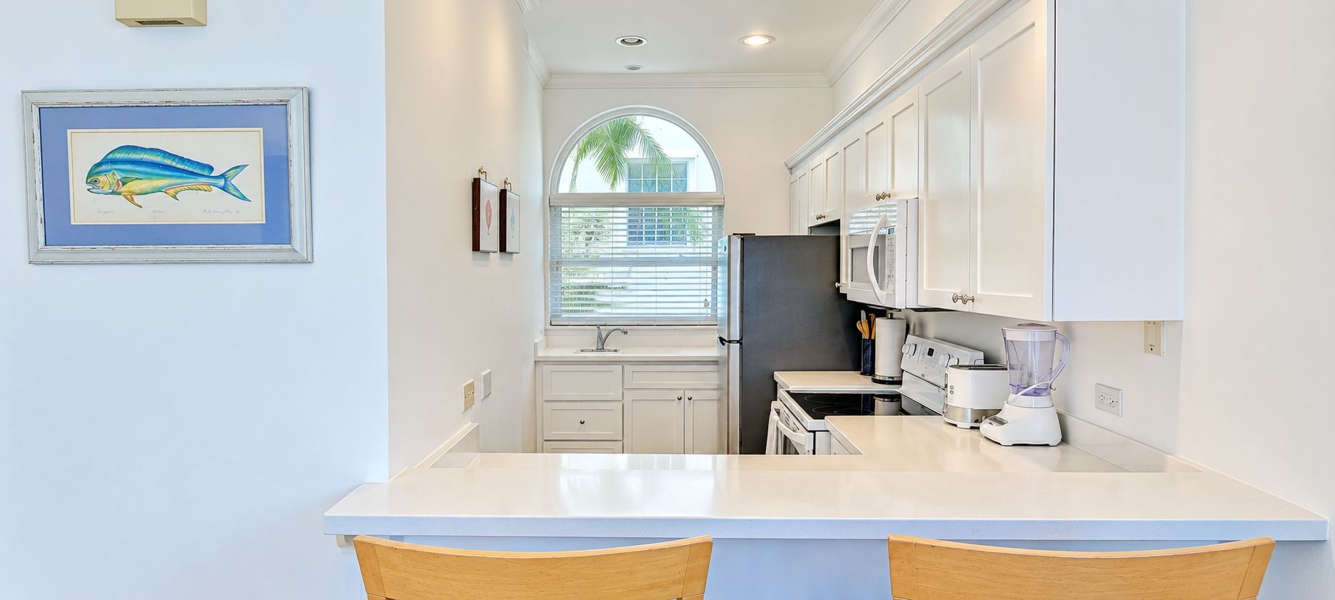 A compact kitchen with white cabinets, a built-in oven, a refrigerator, and a blender on the counter.
