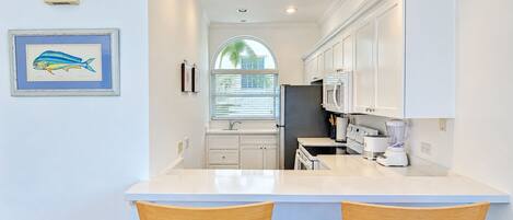 A compact kitchen with white cabinets, a built-in oven, a refrigerator, and a blender on the counter.