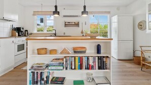 Une cuisine moderne avec des meubles blancs, un plan de travail en bois et une bibliothèque intégrée remplie de livres.