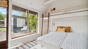 Une chambre avec un lit superposé, une fenêtre donnant sur un paysage verdoyant et une échelle en bois.