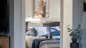 Quarto com cama, travesseiros, mesa de cabeceira, bandeja com uma caneca e um quadro de um cavalo na parede.