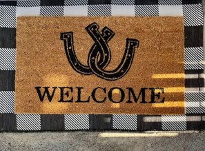 A welcome mat with a horseshoe and the word "WELCOME" on a checkered floor.