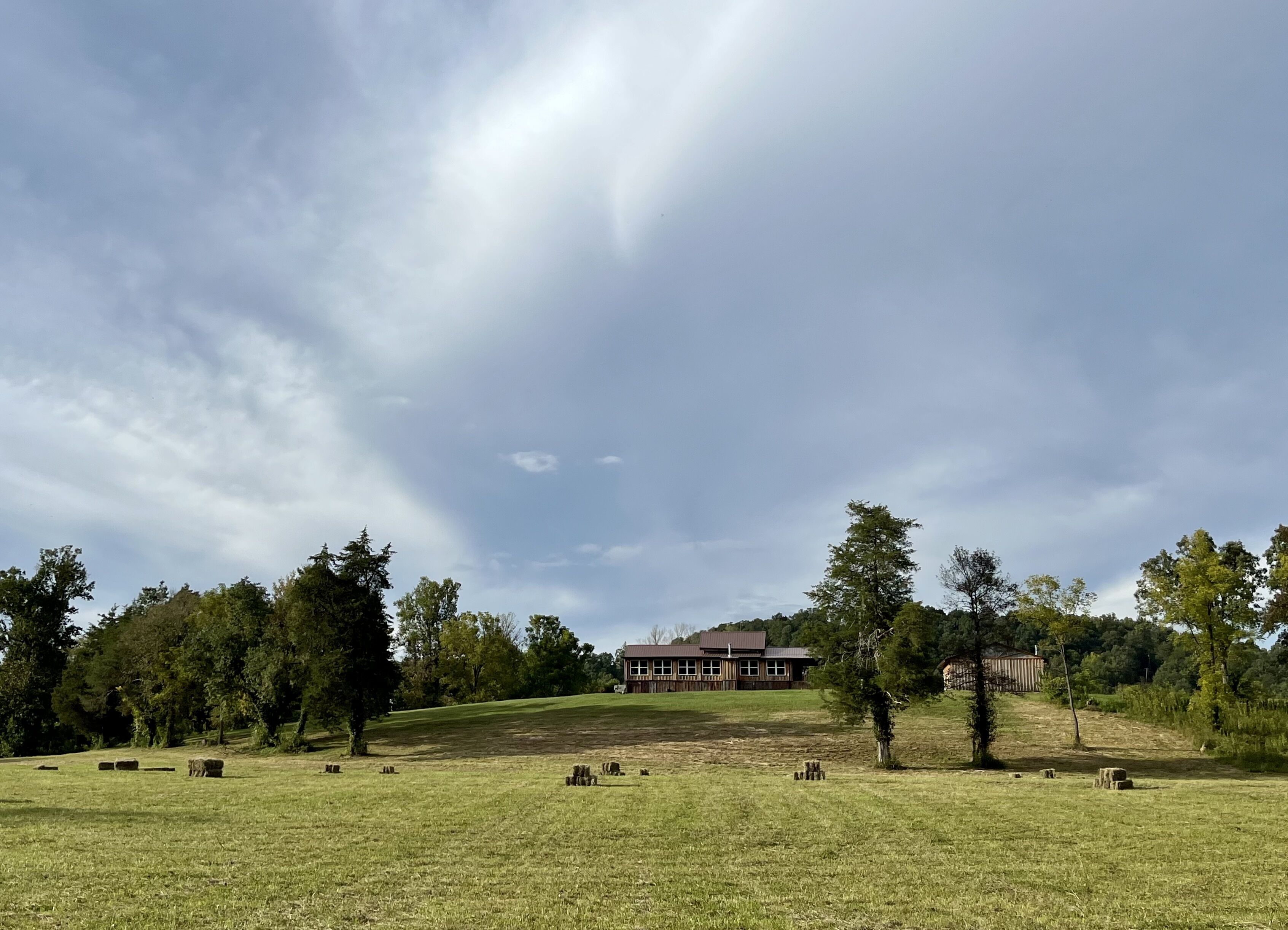 Een landelijk landschap met een groot huis op een heuvel, omringd door bomen en open velden.