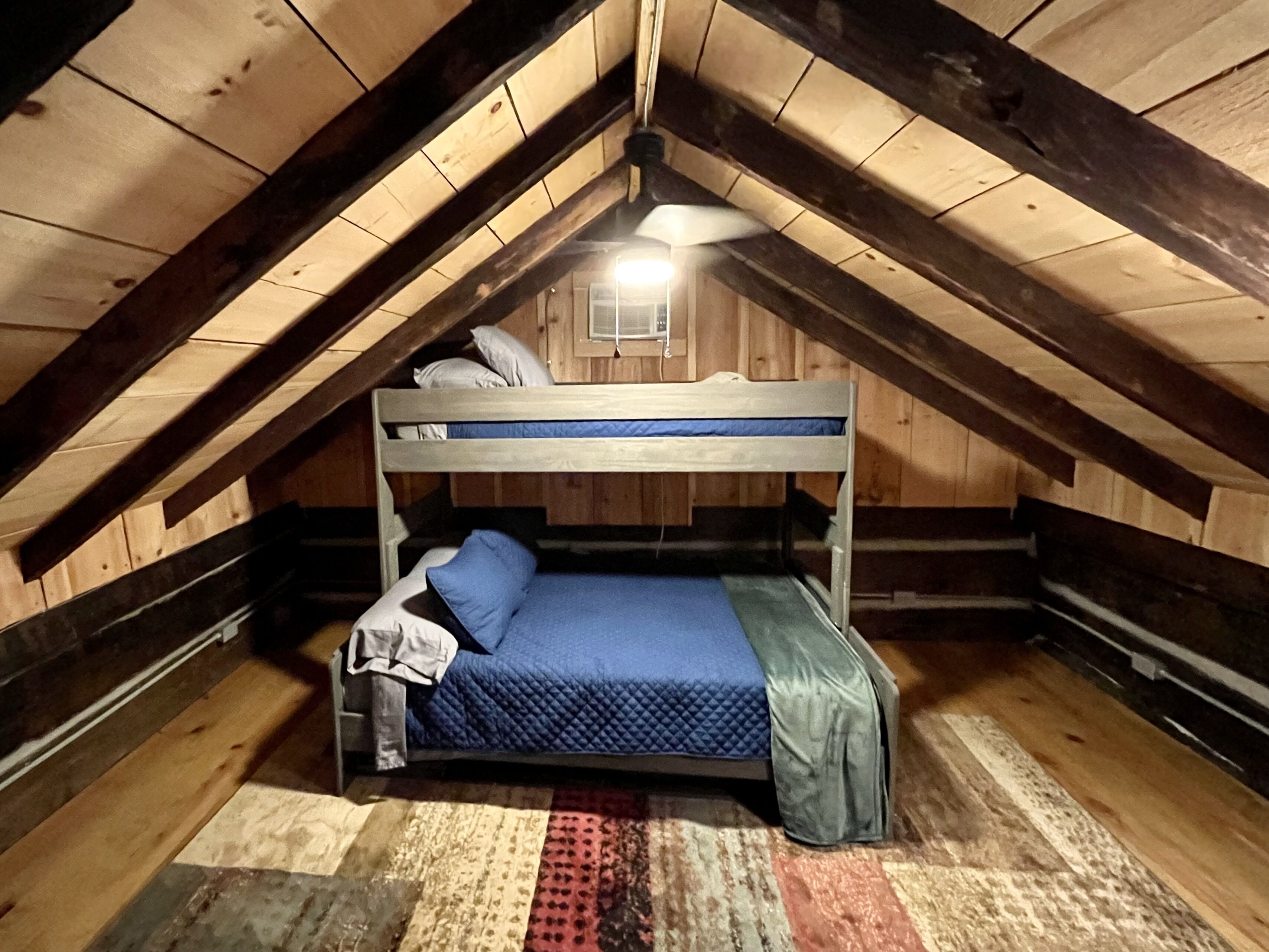 Una piccola e accogliente camera da letto in mansarda, con un letto a castello, pareti in legno e soffitto spiovente.