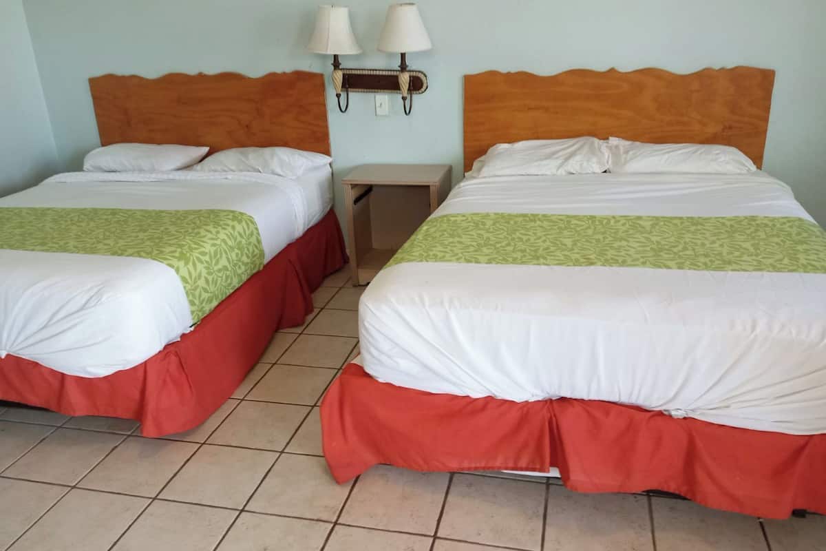 Two double beds with red and green bedspreads, wooden headboards, and two wall-mounted lamps.