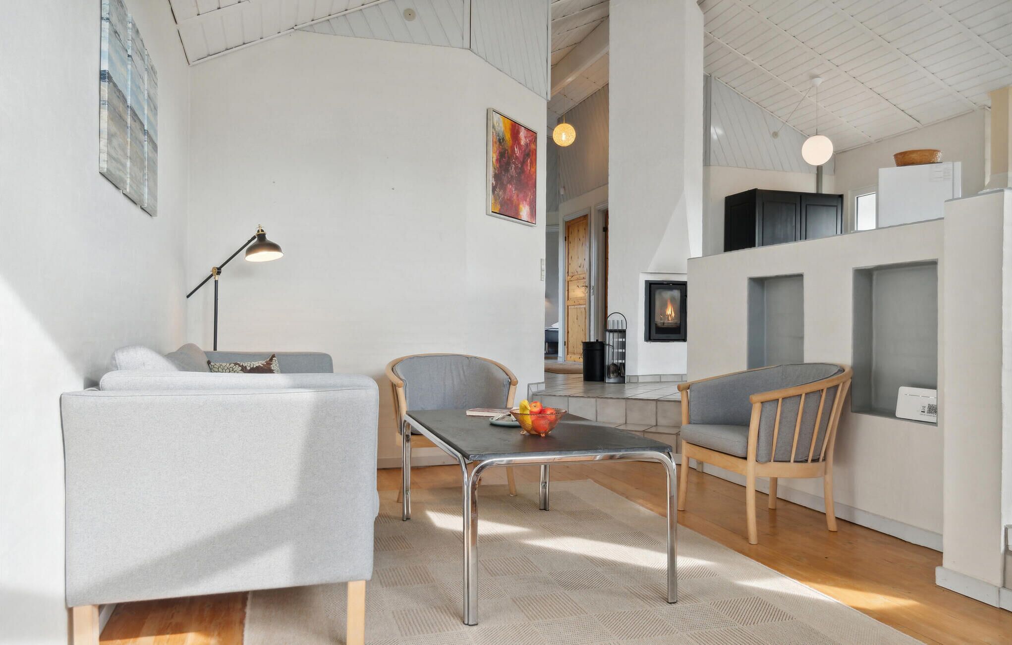 Un espace de vie moderne comprenant un coin repas, un canapé, une table avec un saladier de fruits et une cheminée.