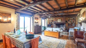 Un coin repas avec une table en bois dressée pour le repas, une cheminée et une bibliothèque avec des étagères.