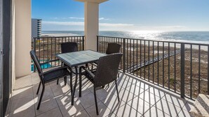A balcony with a table and chairs, overlooking a beach and ocean.