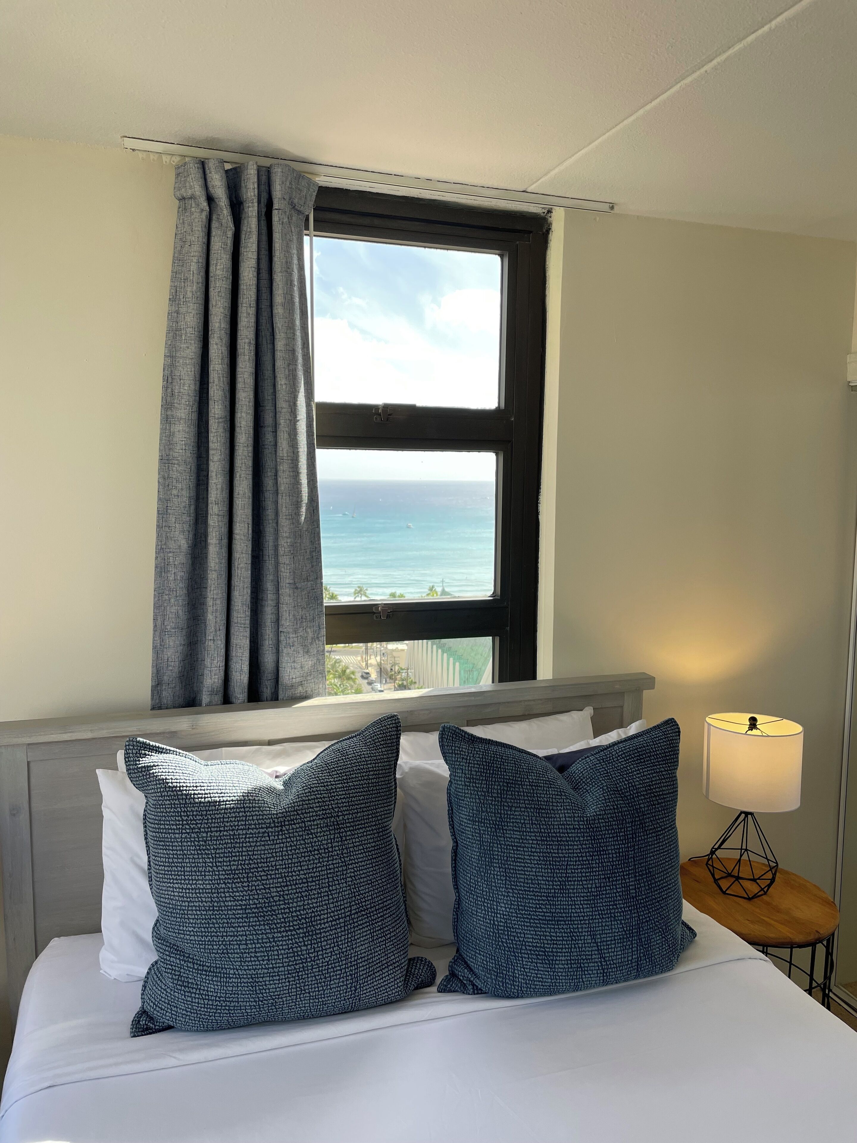 A hotel room with a bed, a view of the ocean, and a lamp on a side table.