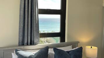 A hotel room with a bed, a view of the ocean, and a lamp on a side table.