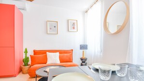 Una sala de estar moderna con un sofá naranja brillante, un espejo redondo y dos obras de arte enmarcadas en la pared.