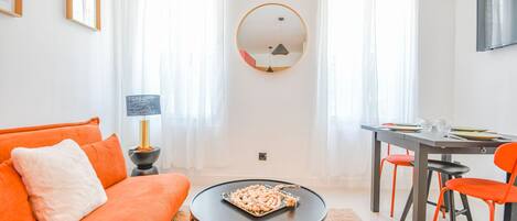 Una sala de estar moderna con un sofá, una mesa de centro, una mesa de comedor con sillas y un espejo redondo en la pared.