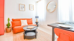 Una sala de estar luminosa con un sofá, una mesa redonda y una zona de comedor con una silla y platos.