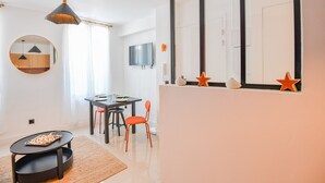 Una habitación moderna y luminosa con una mesa de comedor, sillas, un espejo redondo y un televisor montado en la pared.