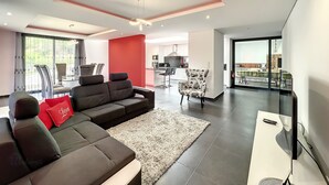 A modern living room with a sectional sofa, a red accent wall, and a view of the kitchen and dining area. - Dream House 2, by LSA Madeira (Calheta)