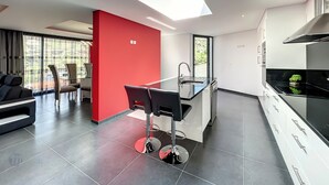 A modern kitchen with a skylight, a dining area with chairs, and a red accent wall. - Dream House 2, by LSA Madeira (Calheta)