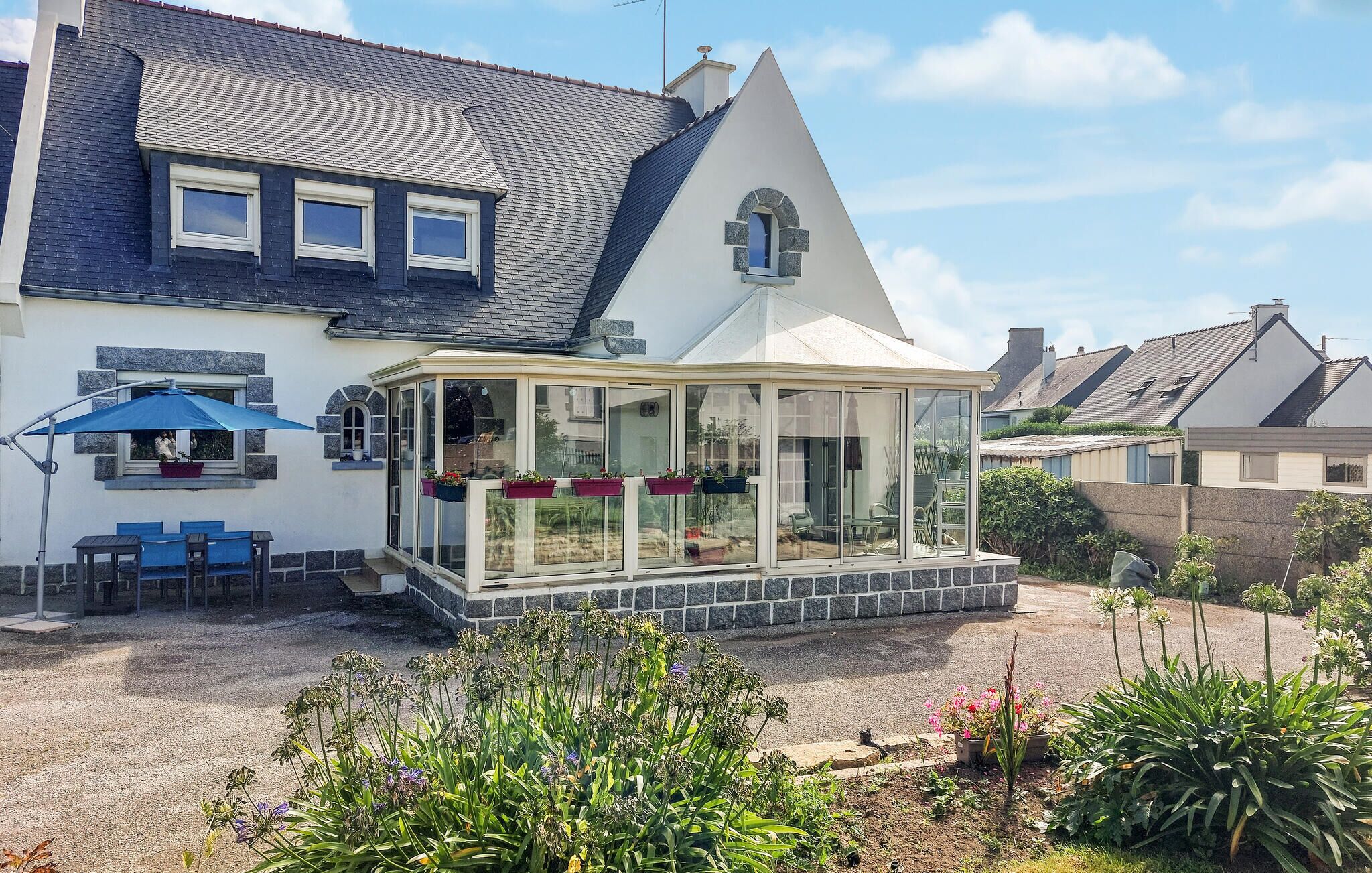Una casa con un invernadero, un patio con mobiliario exterior y un jardín con diversas plantas.