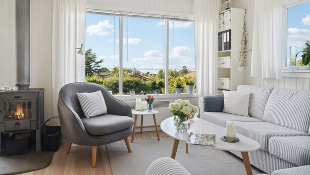 A cozy living room with a fireplace, a sofa, a chair, and a view of greenery outside.