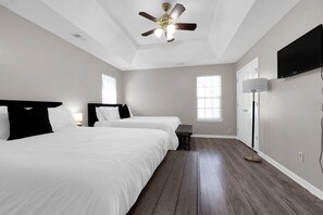 Ein geräumiges Schlafzimmer mit zwei Betten, einem Deckenventilator, einem Fernseher und einer Stehlampe.