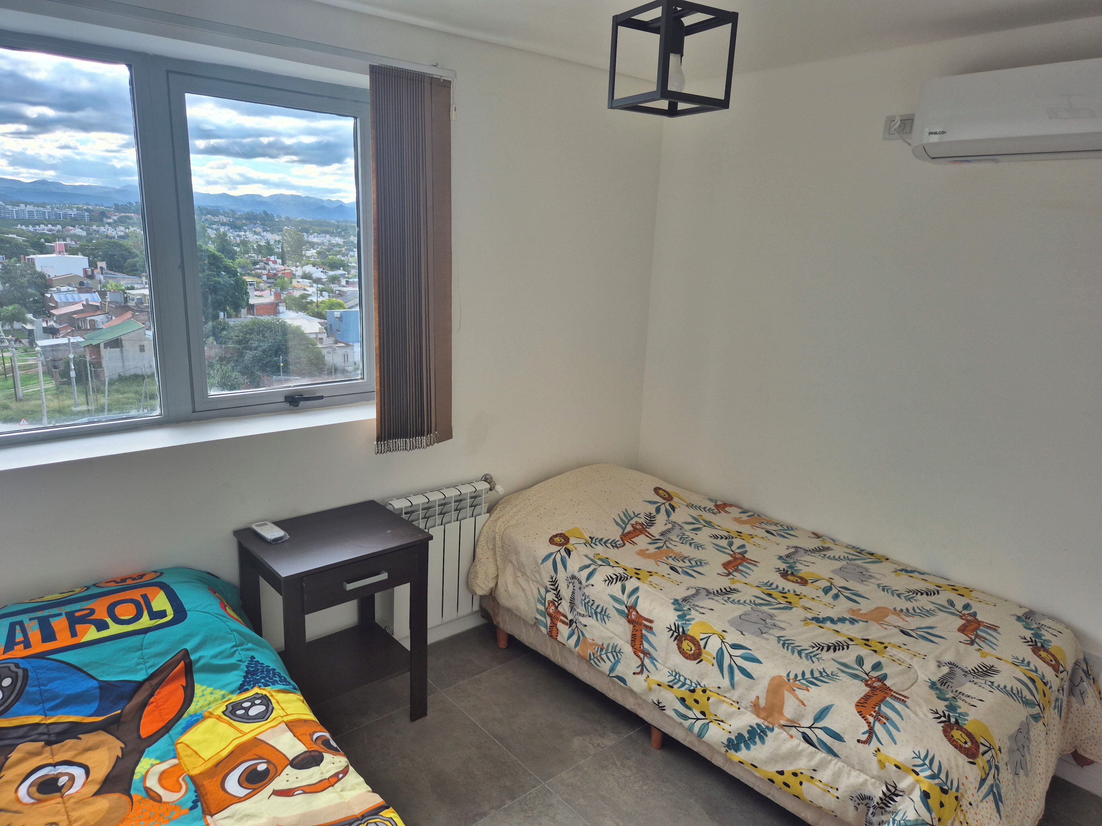 A bedroom with a window, a radiator, a desk, and a bed with a colorful animal print bedspread.