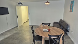 Een eetgedeelte met een ronde houten tafel, zwarte stoelen, een kleine cactusplant en een lijst met een certificaat.