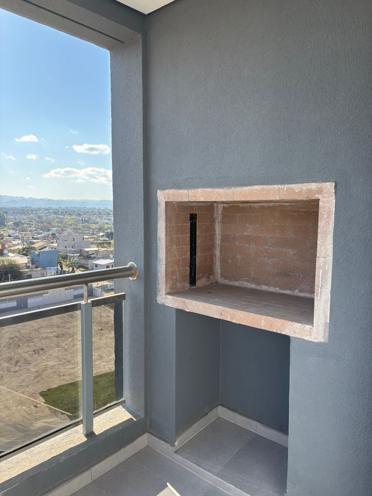 A balcony with a view of a cityscape, a brick fireplace, and a metal railing.