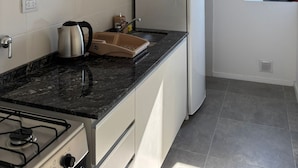 Een moderne keuken met witte kasten, een zwart aanrecht, een fornuis, een koelkast en een raam met uitzicht.