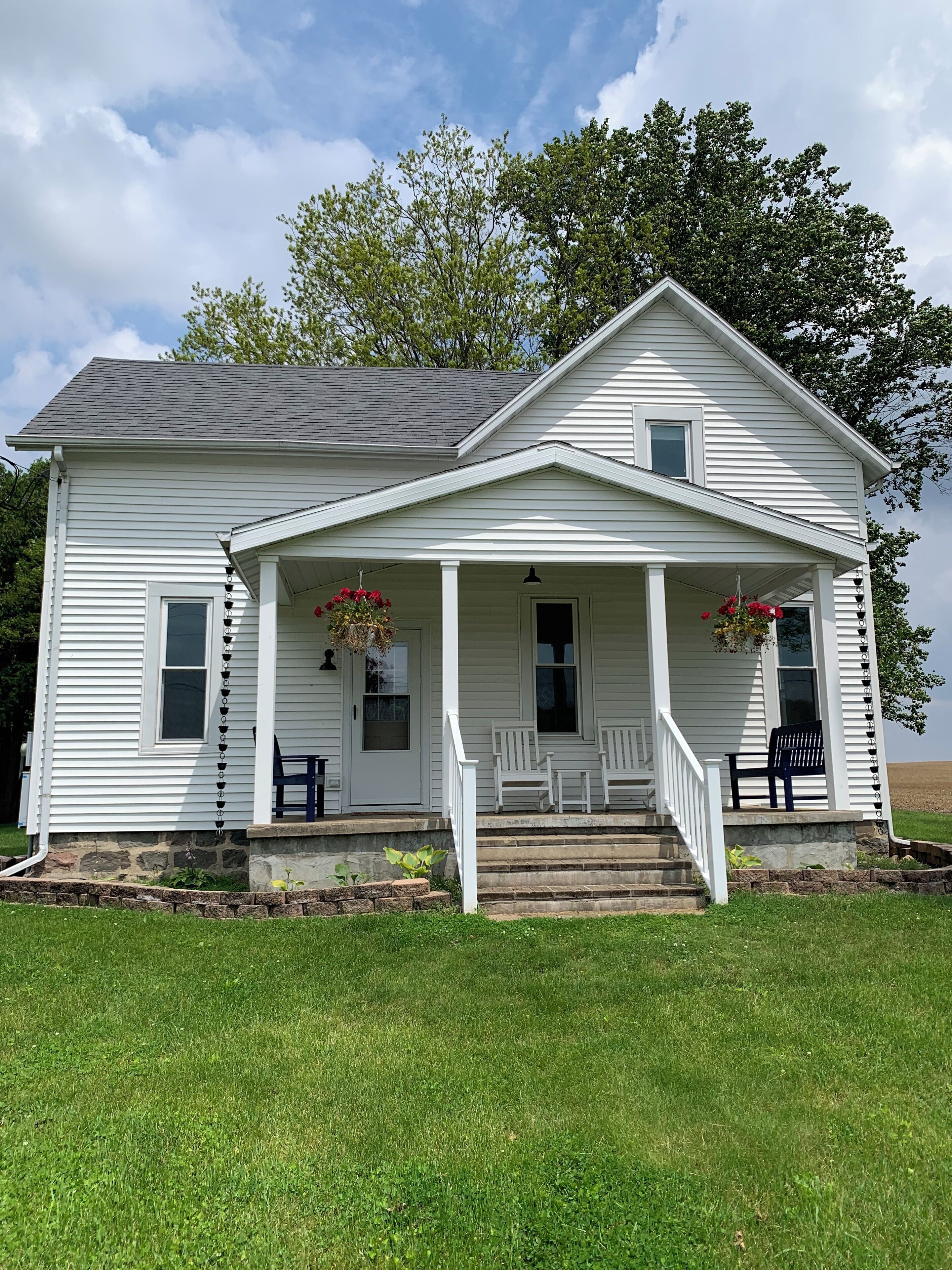 A white two-story house with a porch, stone steps, and hanging flower baskets.