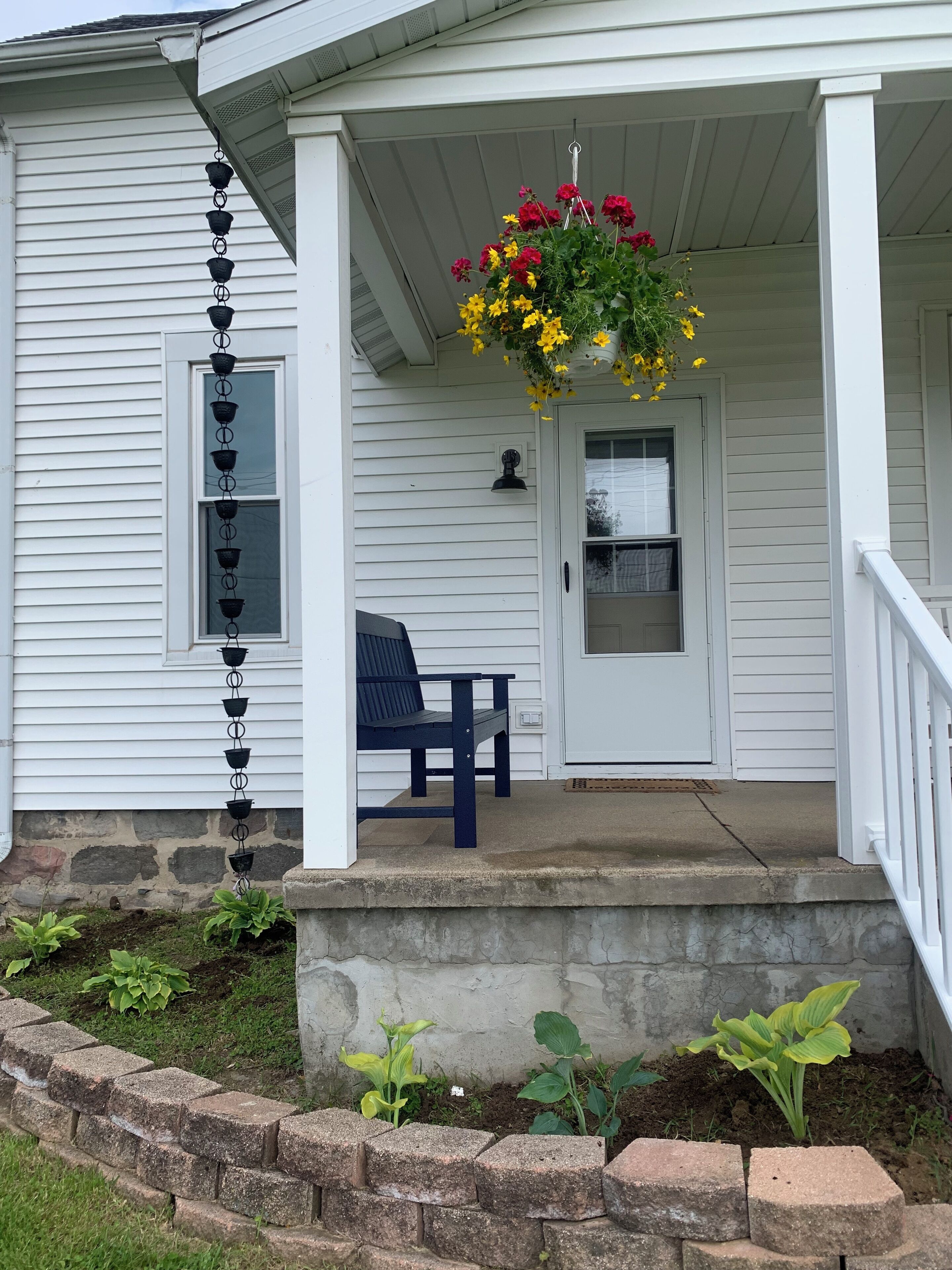 A porch with a hanging flower basket, a bench, and a door with a window.