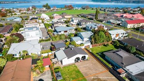 An aerial view of a residential area with houses, a large open field, and a body of water in the background. - Central Inn Taupo (Taupo)