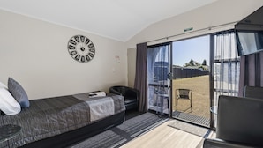 A hotel room with a bed, a chair, a small table, a clock, and a view of the outside. - Central Inn Taupo (Taupo)